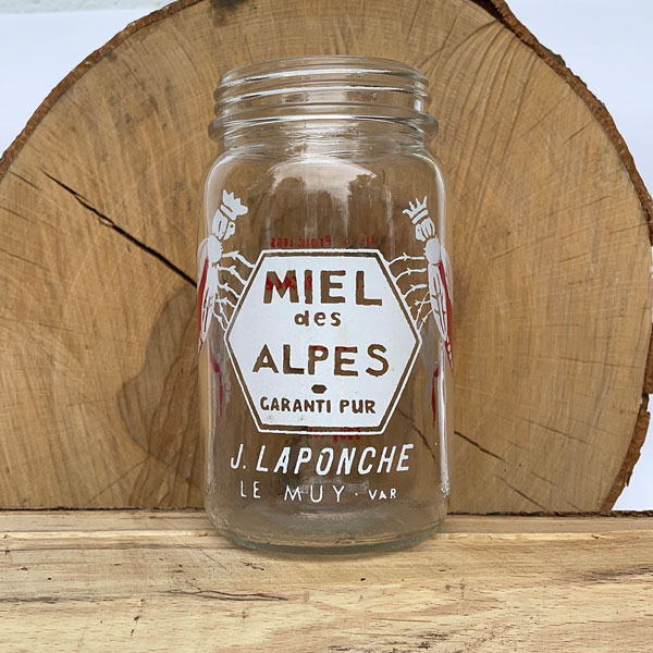 Hübsche Bienenköniginnen rahmen die Wabe mit der Sortenbezeichnung ein Altes Honigglas mit Aufdruck "Miel des Alpes, J. Laponche, Le Muy"